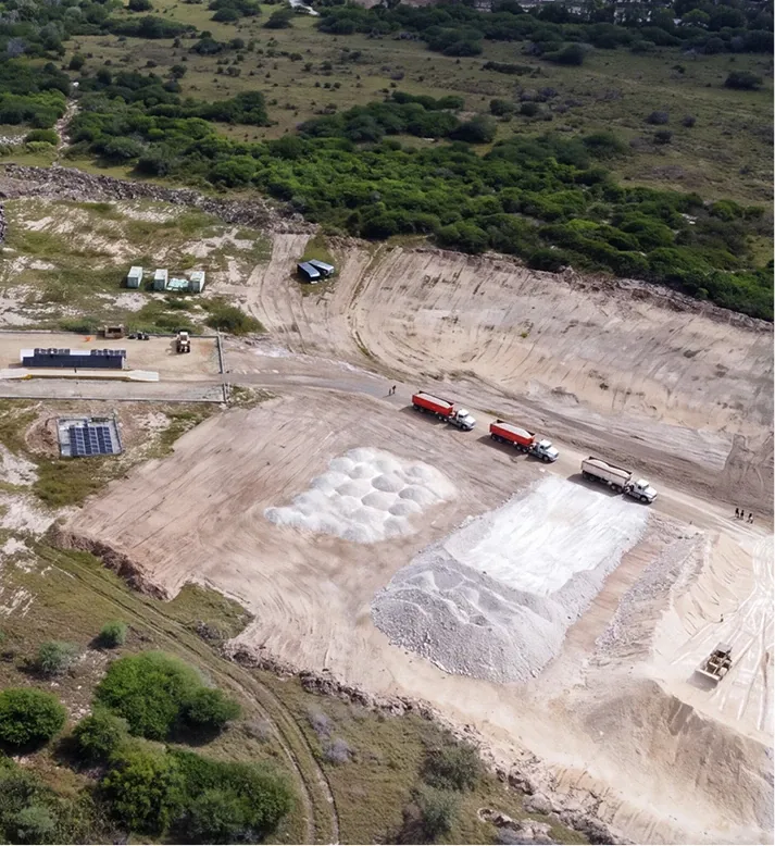 Aerial view of a stockpile yard with cones of white clay, trucks loading beside them and scrub around the cut.