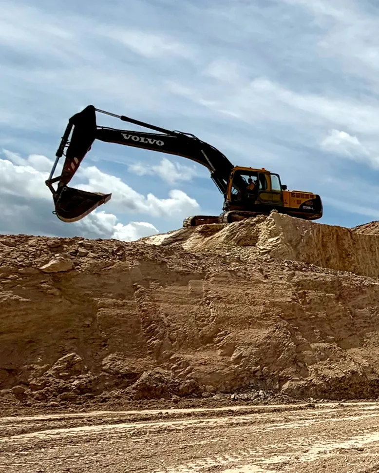 Excavator on top of a cut bench of pale clay, against a cloudy sky.