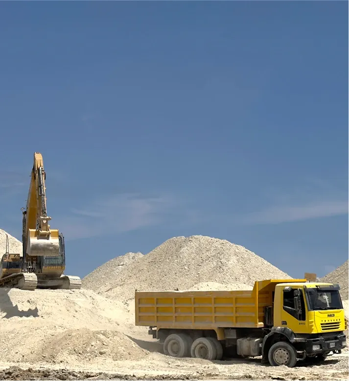 Excavator and tipper truck working between stockpiles of white clay.