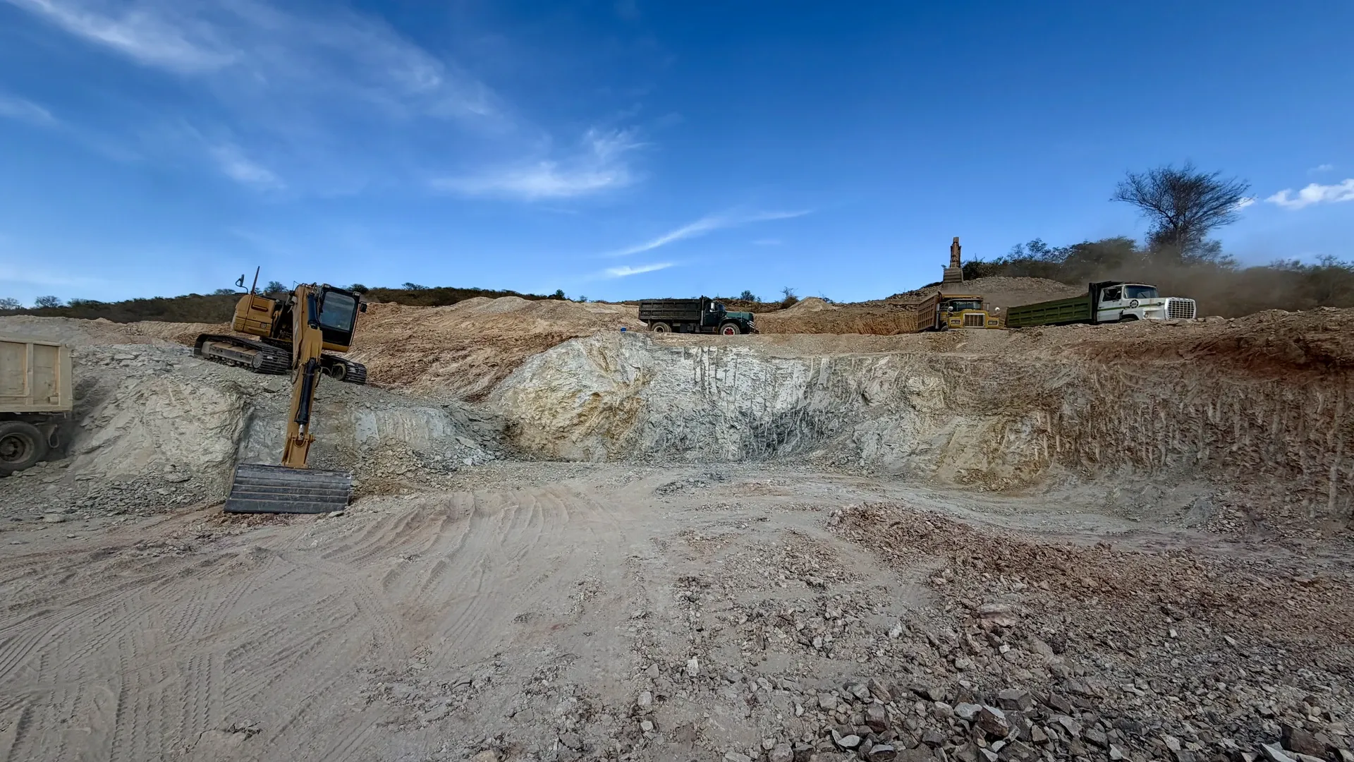 Excavator at a white clay face, with trucks waiting on the bench above.