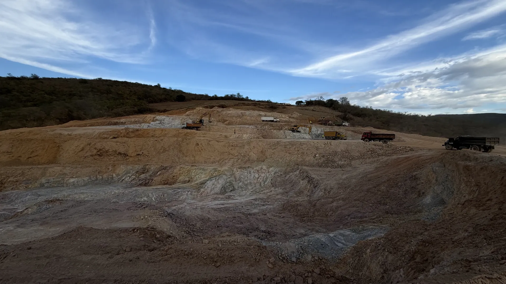Open-pit clay quarry cut in benches across a hillside, with excavators and trucks on the upper levels.