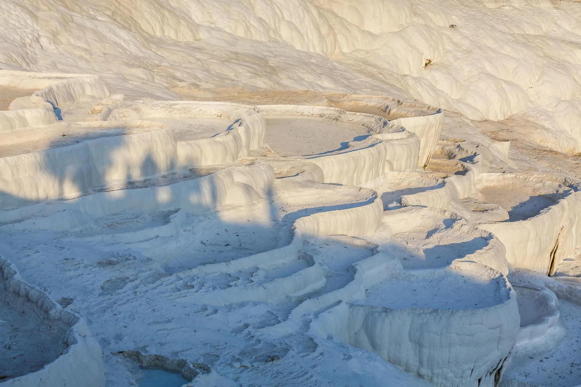 White travertine terraces with shallow pools, in low sunlight.