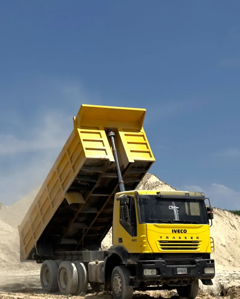 Tipper truck raising its body beside stockpiles of white clay, against a clear sky.